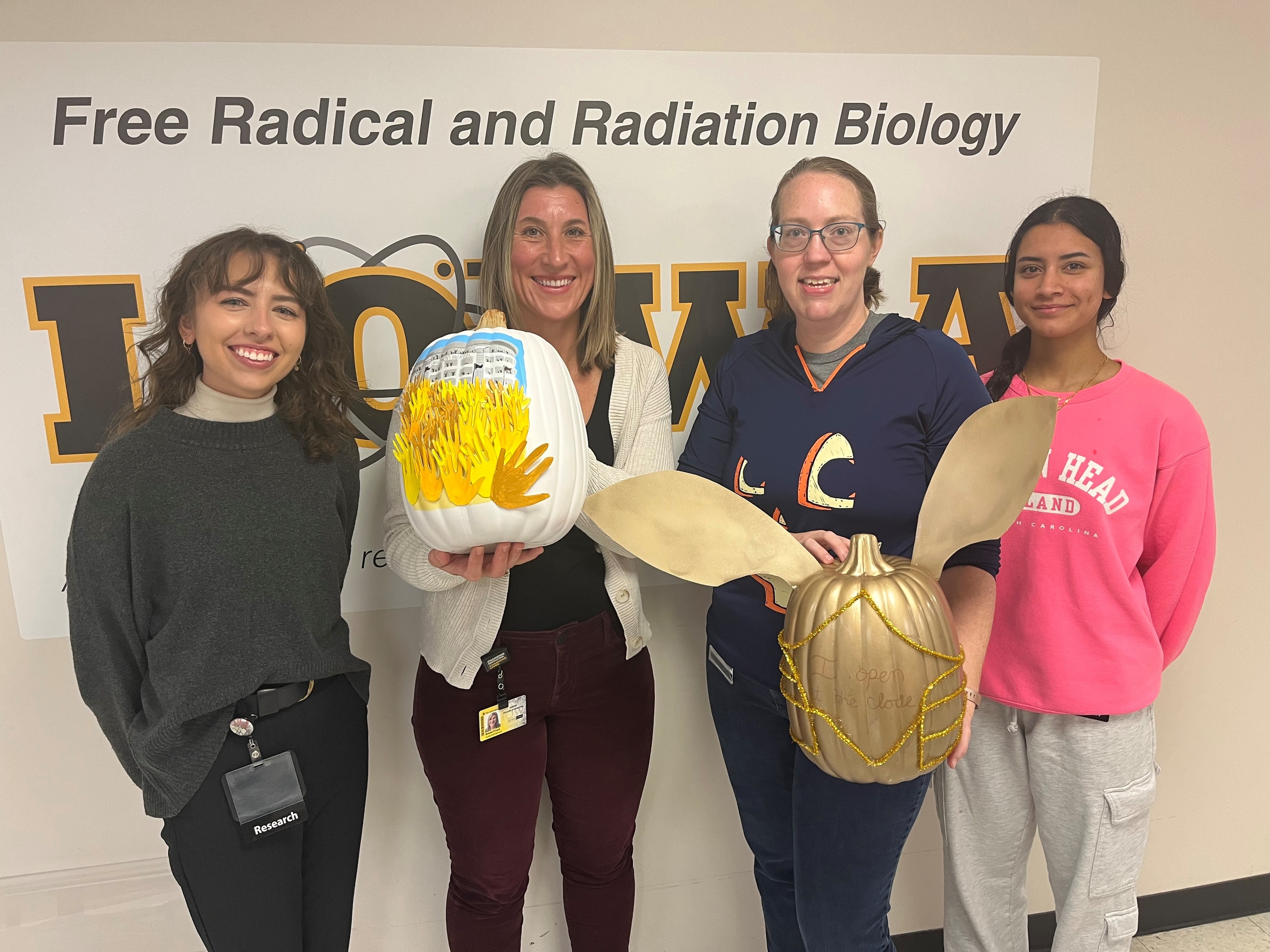 Howard lab members stand in front of a wall, posing with the pumpkins they submitted for the pumpkin decorating contest.