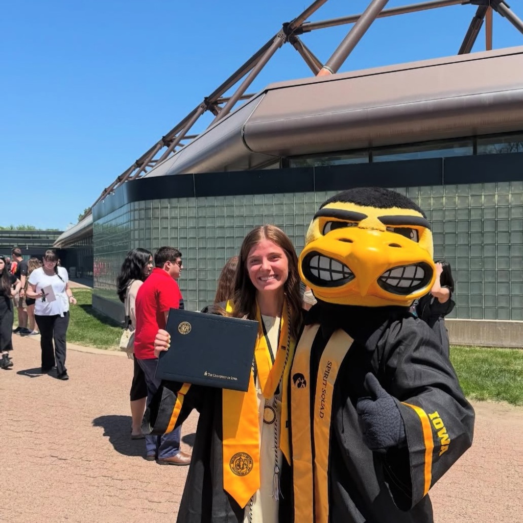 Claire Graham and Iowa's mascot Herky the Hawk pose for a photo, both wearing graduation robes. 