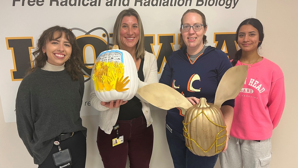 Howard lab members stand in front of a wall, posing with the pumpkins they submitted for the pumpkin decorating contest.